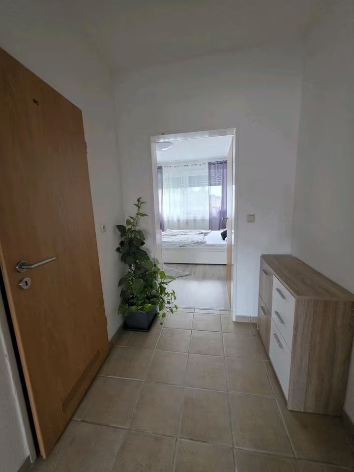 Flur mit Kommode und Pflanze, Blick in ein helles Schlafzimmer mit großem Fenster.