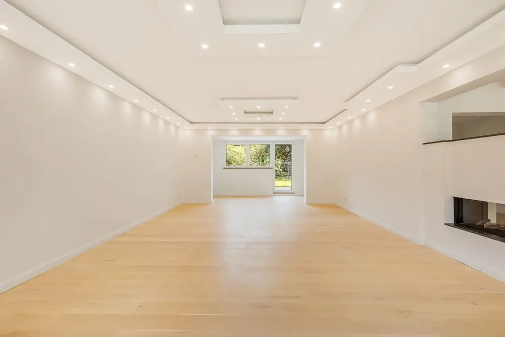 Helles, großes Wohnzimmer mit Holzboden, vielen Deckenlichtern und Fenstertür zum Garten.