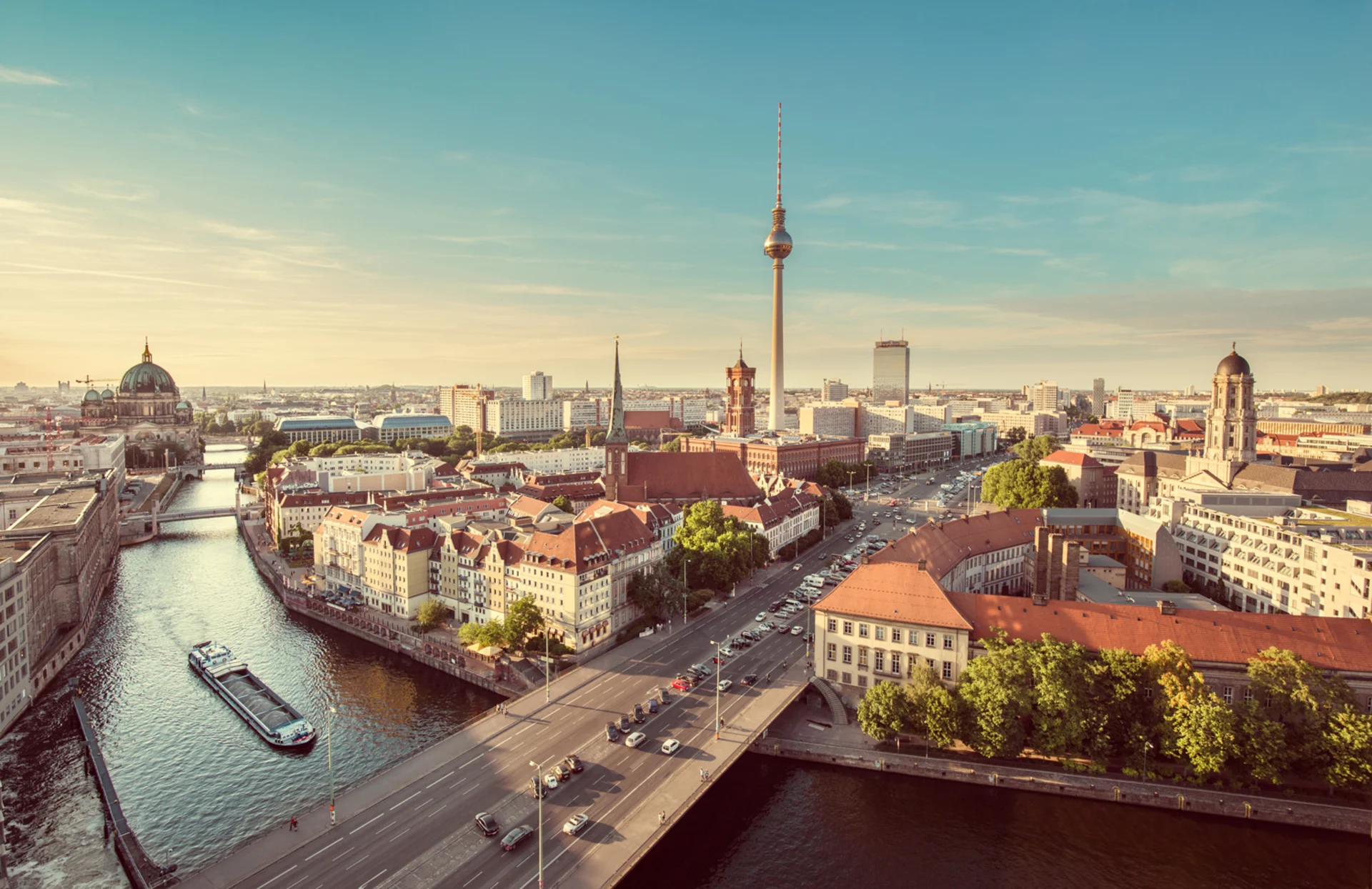 Stadtpanorama mit Fluss, Brücke, Fernsehturm und historischen Gebäuden bei Tageslicht.