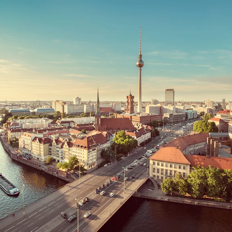 Stadtpanorama mit Fluss, Brücke, Fernsehturm und historischen Gebäuden bei Tageslicht.