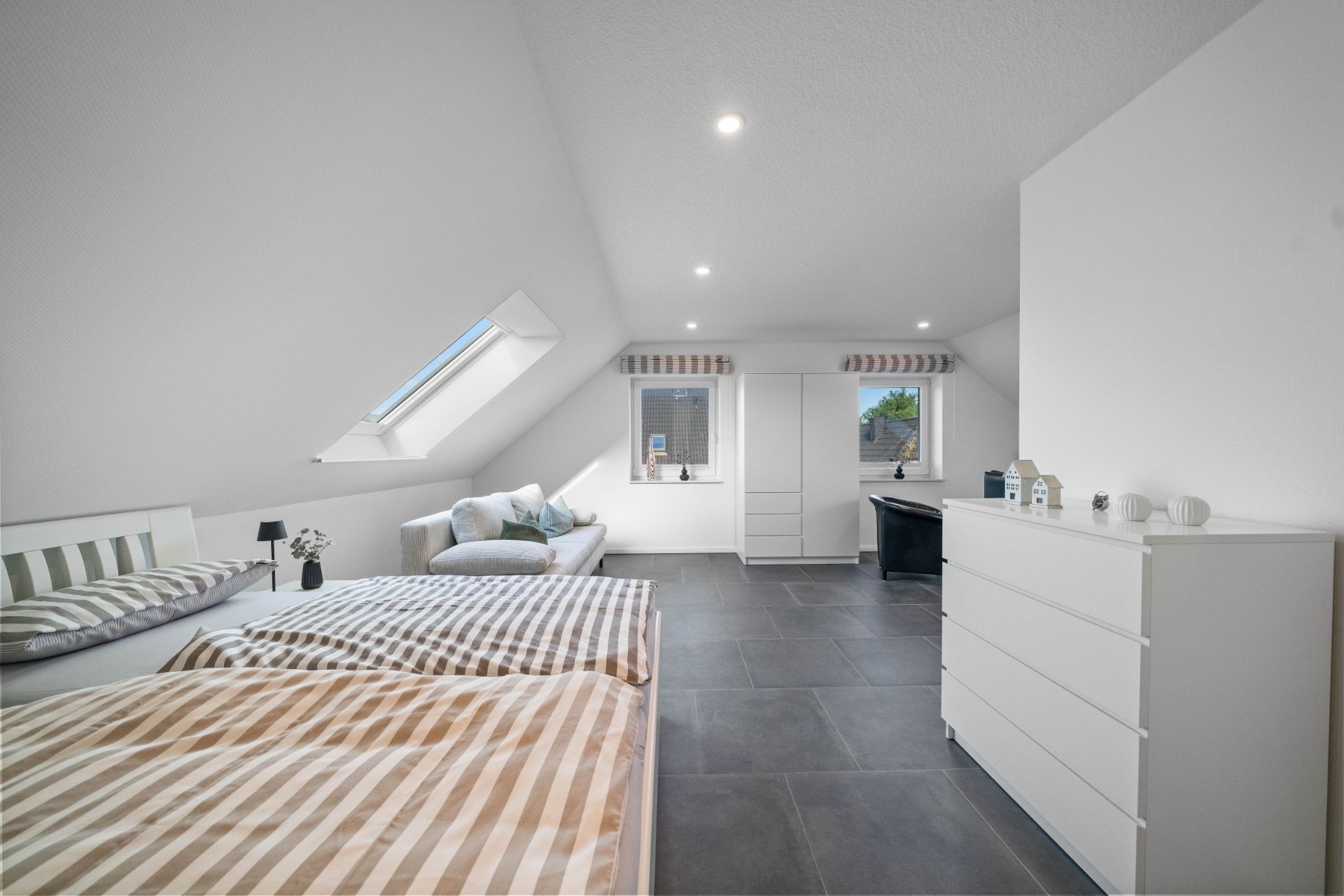 Helles Schlafzimmer mit Dachfenster, Doppelbett, Sofa, Kommode und Schreibtisch.