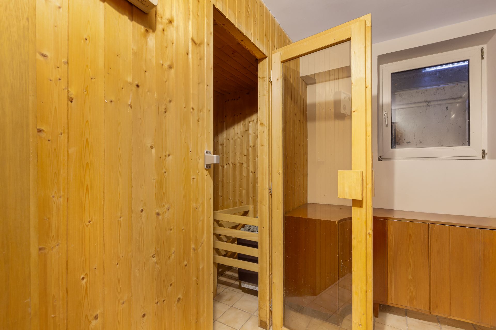 Kleine Sauna mit Glastür, Holzwänden und Fenster in einem Raum.