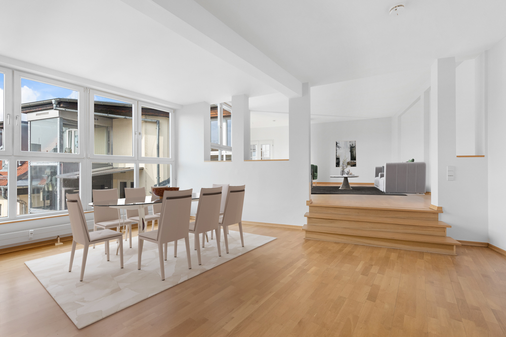 Helles Esszimmer mit großem Fenster, Essgruppe und erhöhtem Wohnbereich mit Sofa.