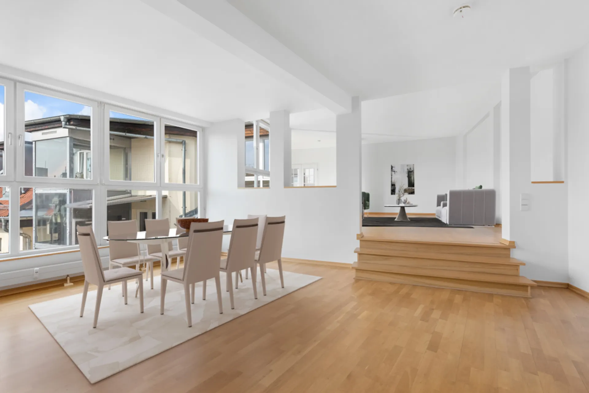 Helles Esszimmer mit großem Fenster, Essgruppe und erhöhtem Wohnbereich mit Sofa.