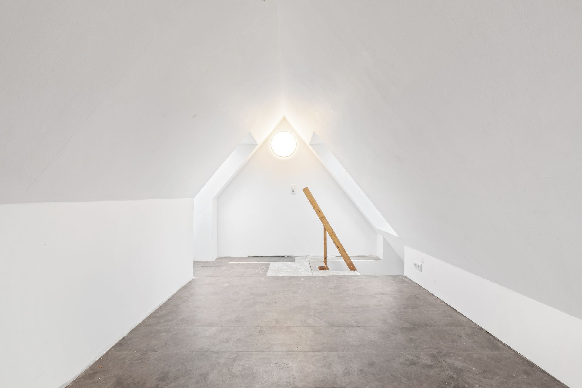 Heller Dachbodenraum mit weiß gestrichenen Wänden, Rundfenster und Treppenöffnung.