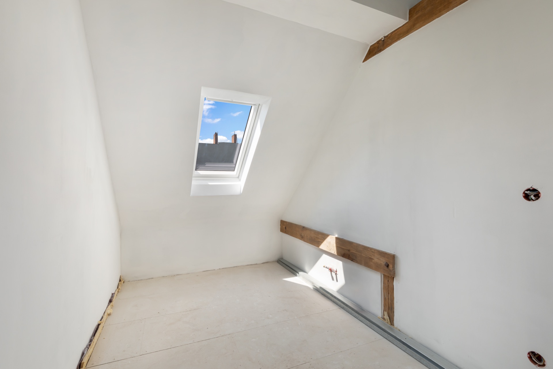Heller Raum mit schräger Decke, Dachfenster und sichtbarem Holzbalken.
