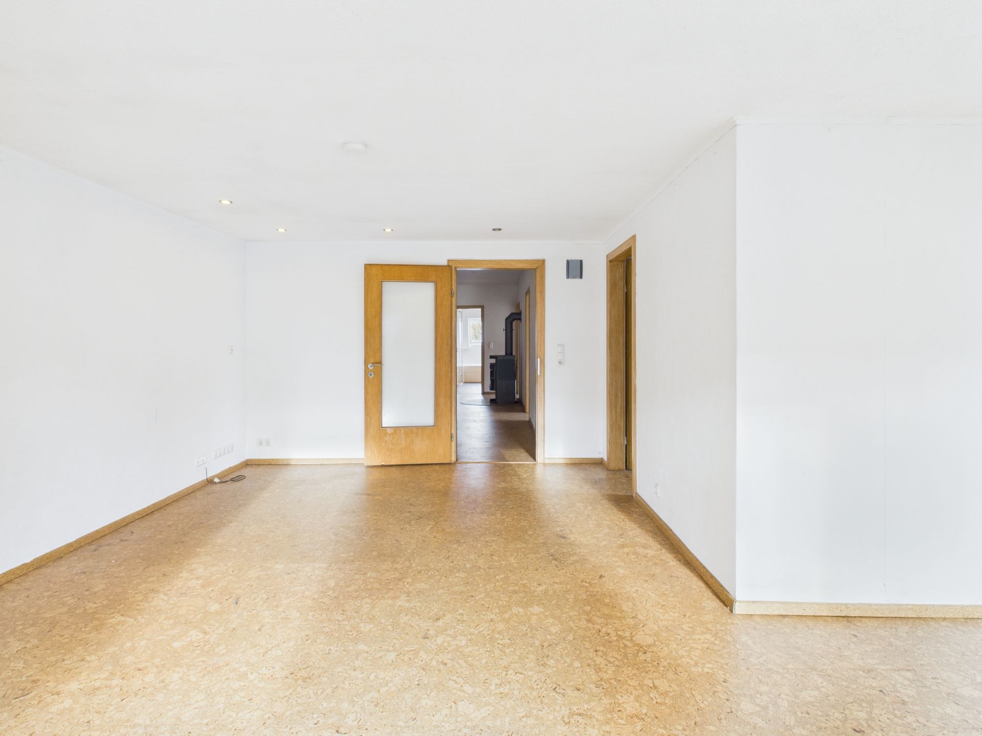 Leeres, helles Zimmer mit Holztür und weiß gestrichenen Wänden.