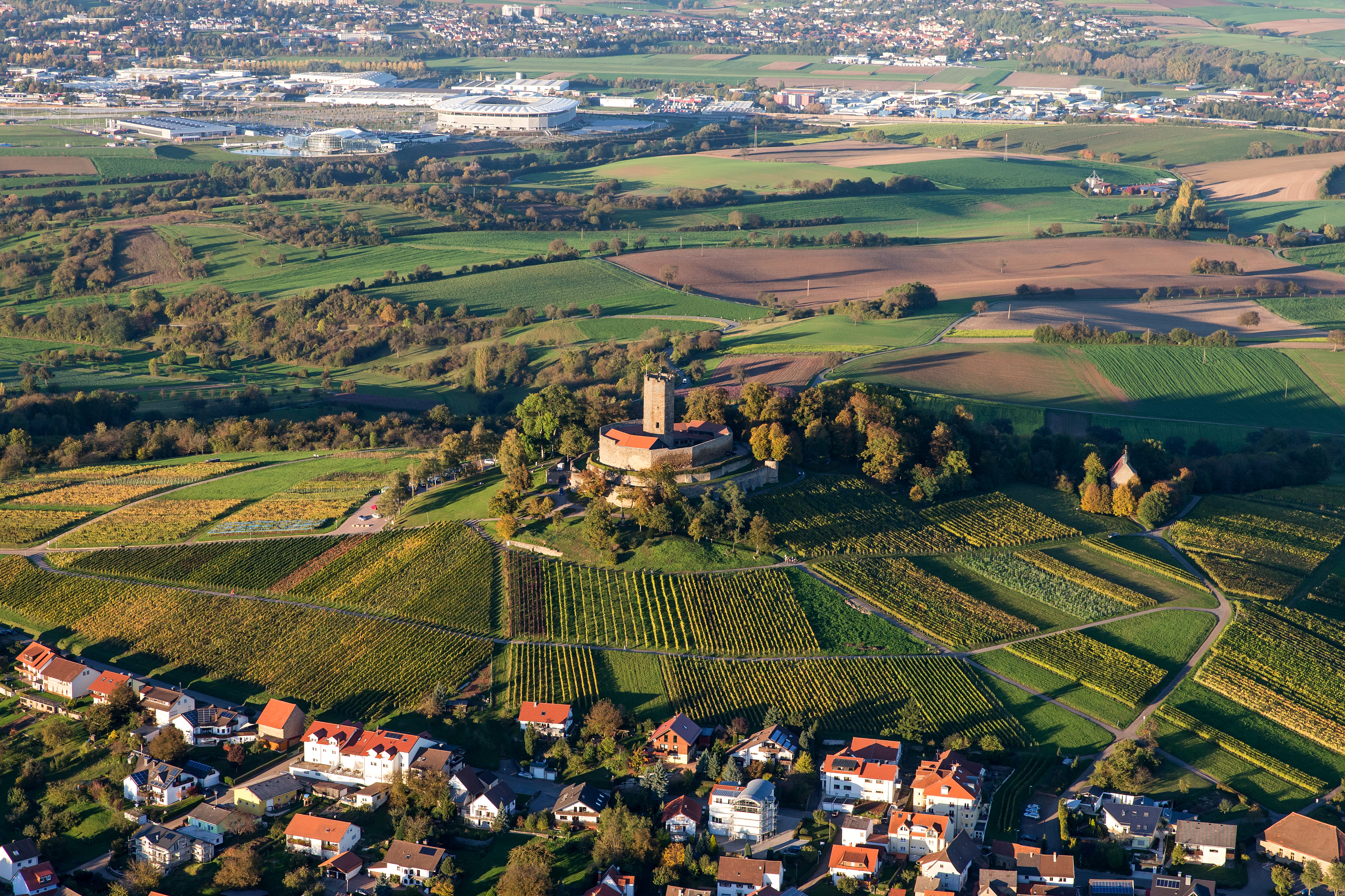 Luftaufnahme von Weinbergen, einem Schloss auf einem Hügel und angrenzenden Wohnhäusern.