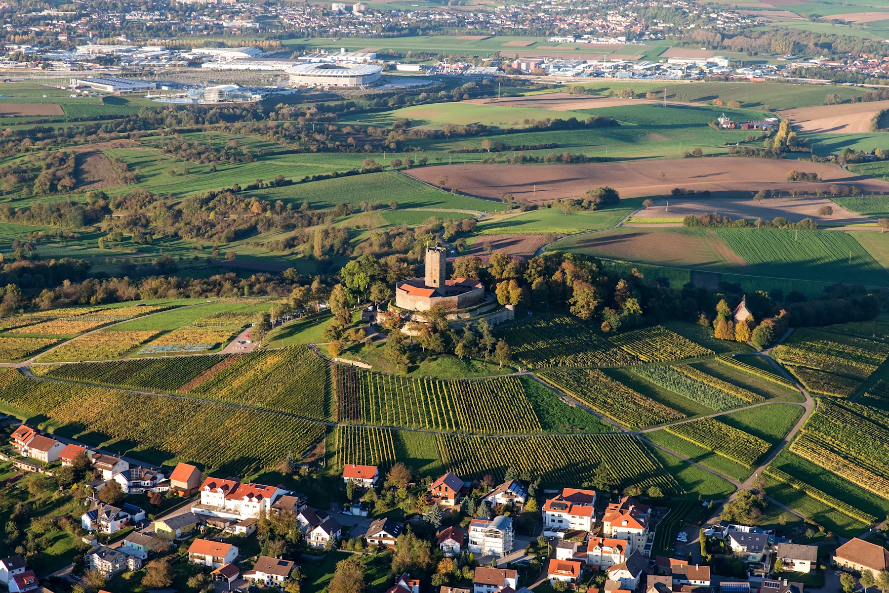 Luftaufnahme von Weinbergen, einem Schloss auf einem Hügel und angrenzenden Wohnhäusern.