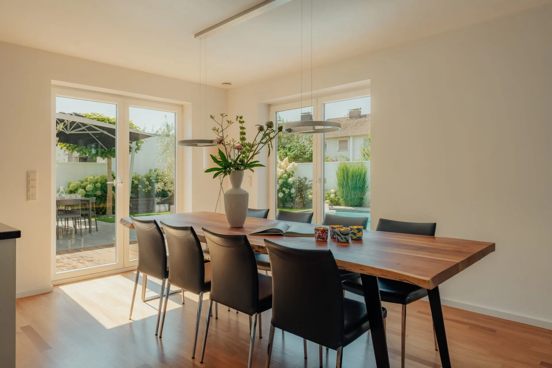 Esszimmer mit Holz-Tisch, schwarzen Stühlen und großer Fensterfront mit Blick in den Garten.