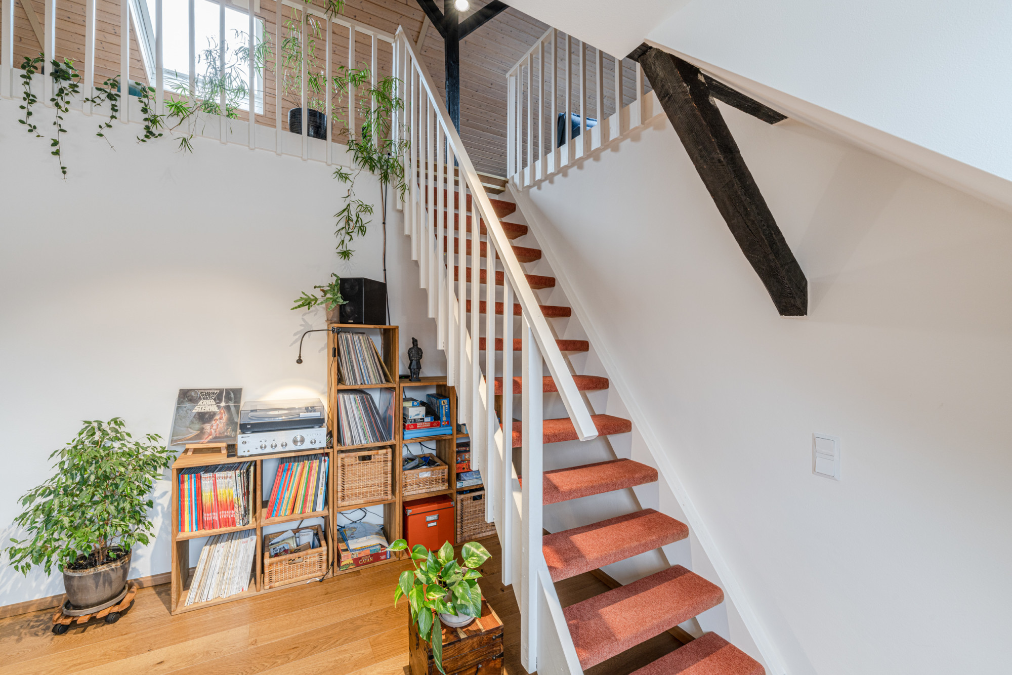 Weiße Treppe mit rotem Teppich, Pflanzen und Regal mit Büchern und Schallplatten.