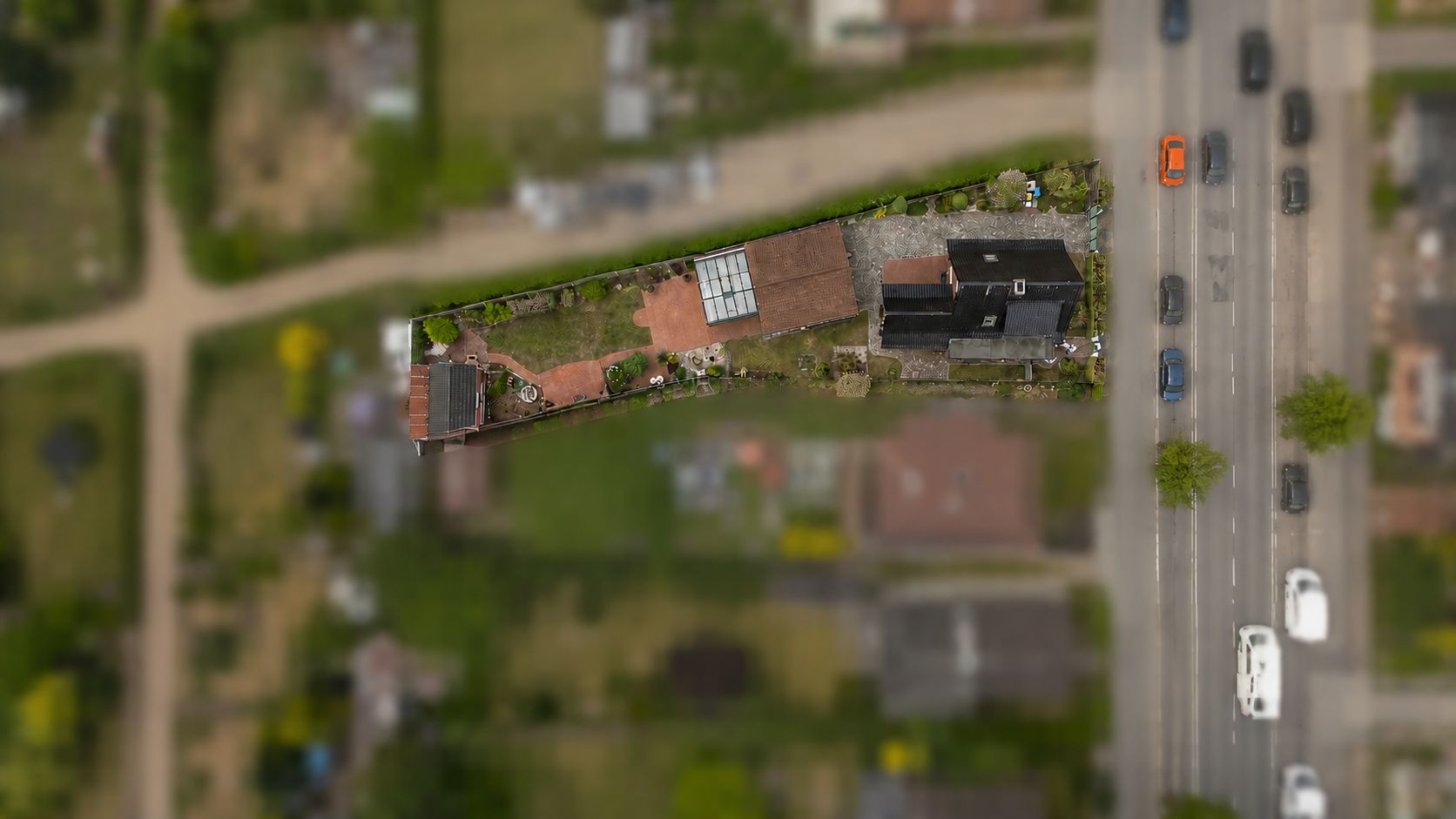 Luftaufnahme eines Wohnhauses mit Garten an einer vielbefahrenen Straße.