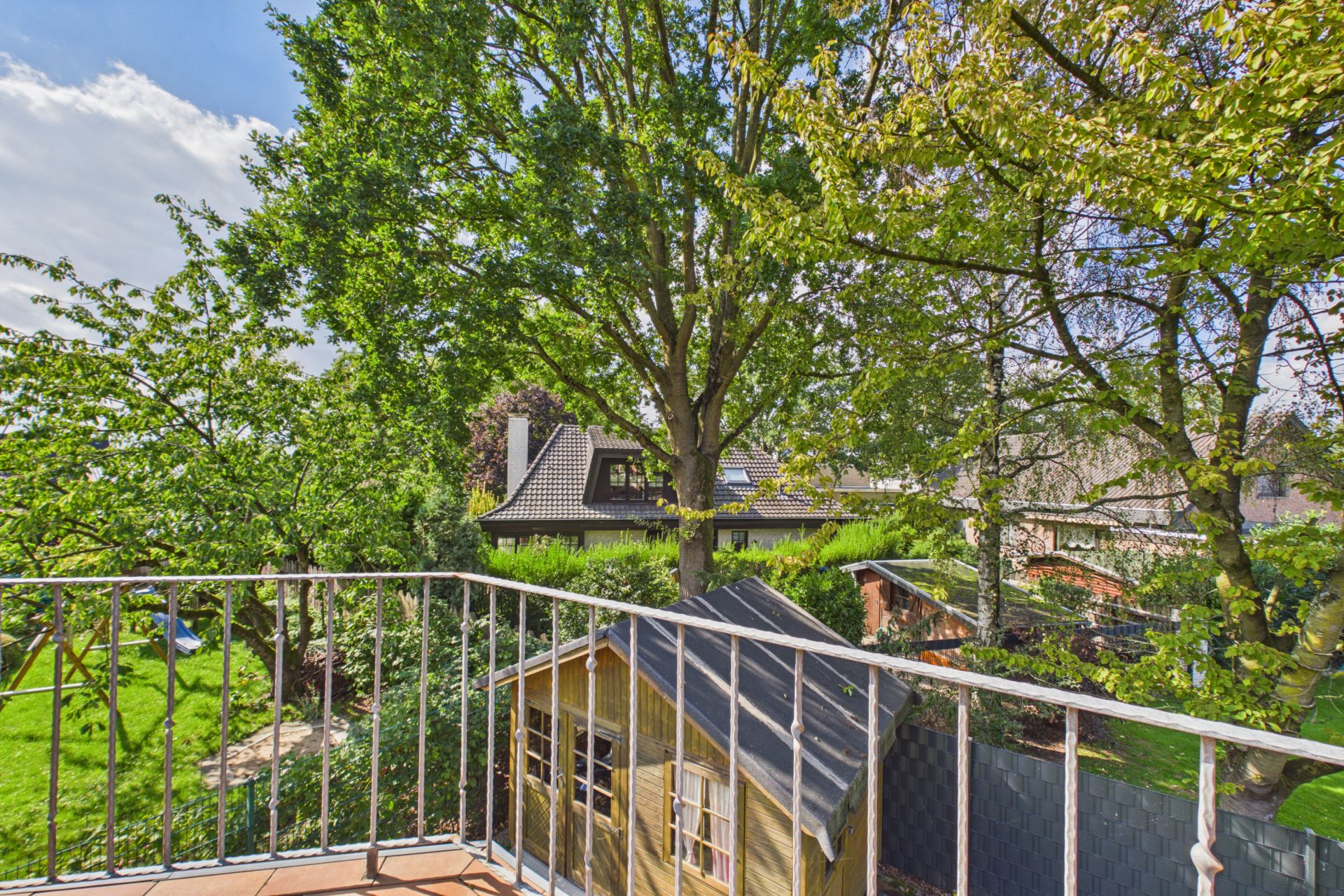 Blick von einem Balkon auf einen Garten mit Bäumen und einem kleinen Holzhaus.