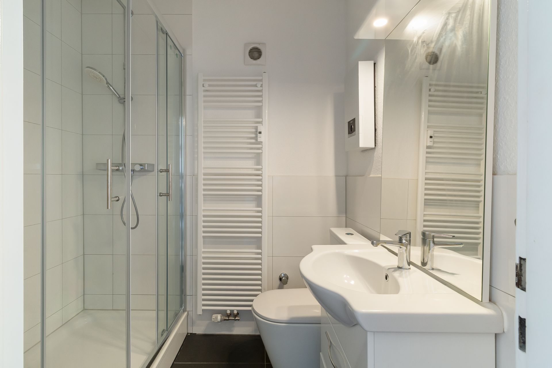 Modernes Badezimmer mit Dusche, Waschbecken, Spiegel, Toilette und Handtuchheizkörper.