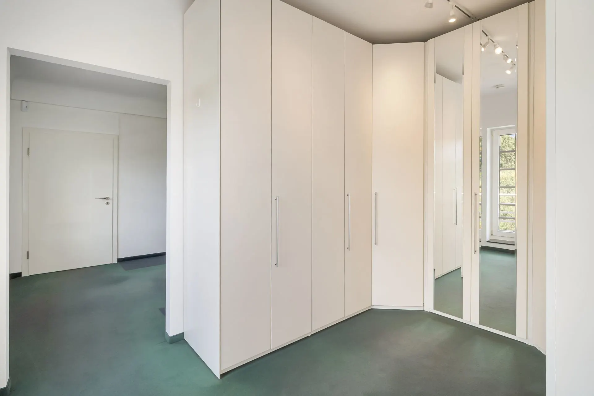 Flur mit großen weißen Einbauschränken und Spiegel, daneben Tür und Fenster.