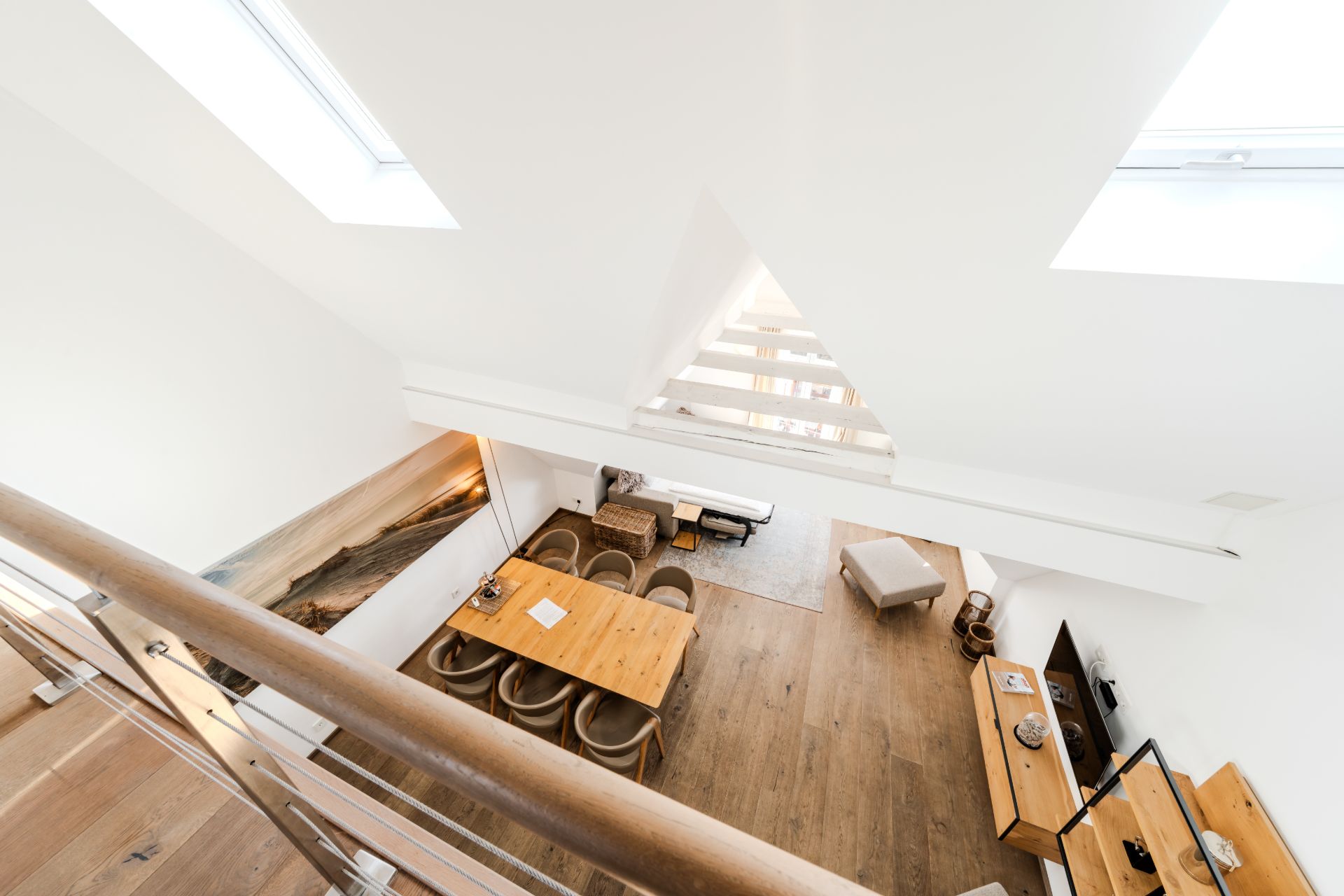 Blick von oben auf ein helles Wohnzimmer mit Holzboden, Esstisch, Stühlen und Sideboards.