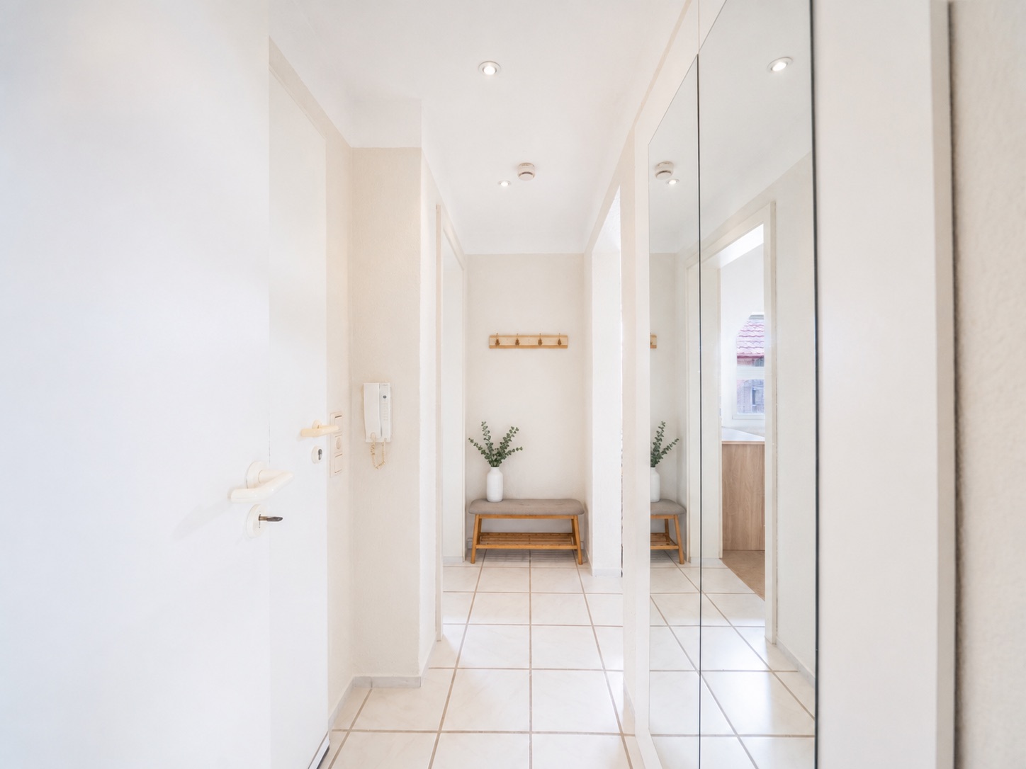Heller Flur mit Spiegel, Bank, Vase und Garderobe an der Wand.
