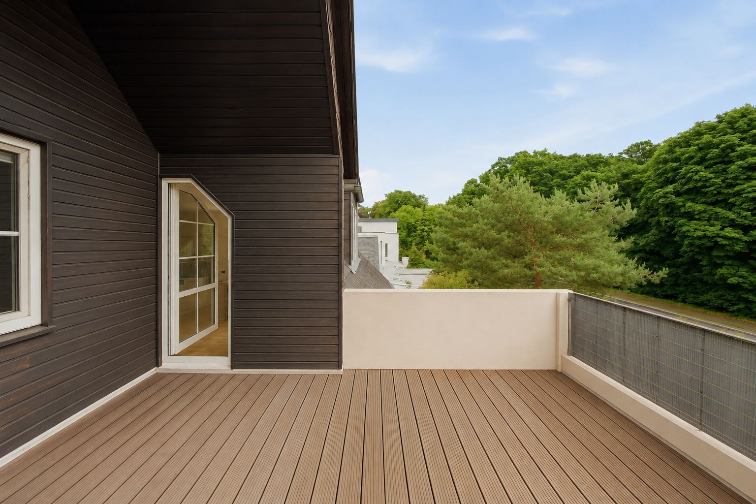 Große Terrasse mit Holzboden, angrenzend an ein dunkles Holzhaus, Blick auf grüne Bäume.