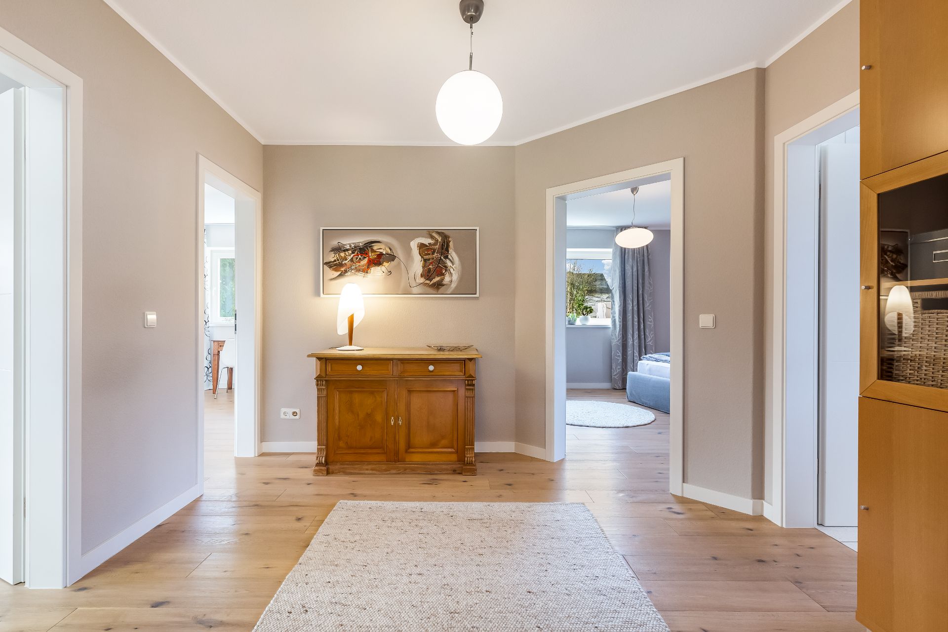 Heller Flur mit Holzkommode, Lampe, Teppich und Türen zu weiteren Räumen.