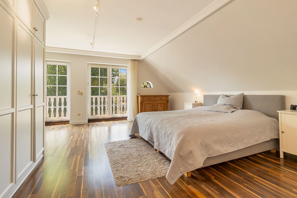 Helles Schlafzimmer mit Doppelbett, Holzboden, Teppich, Schrank und Balkon mit Glastüren.
