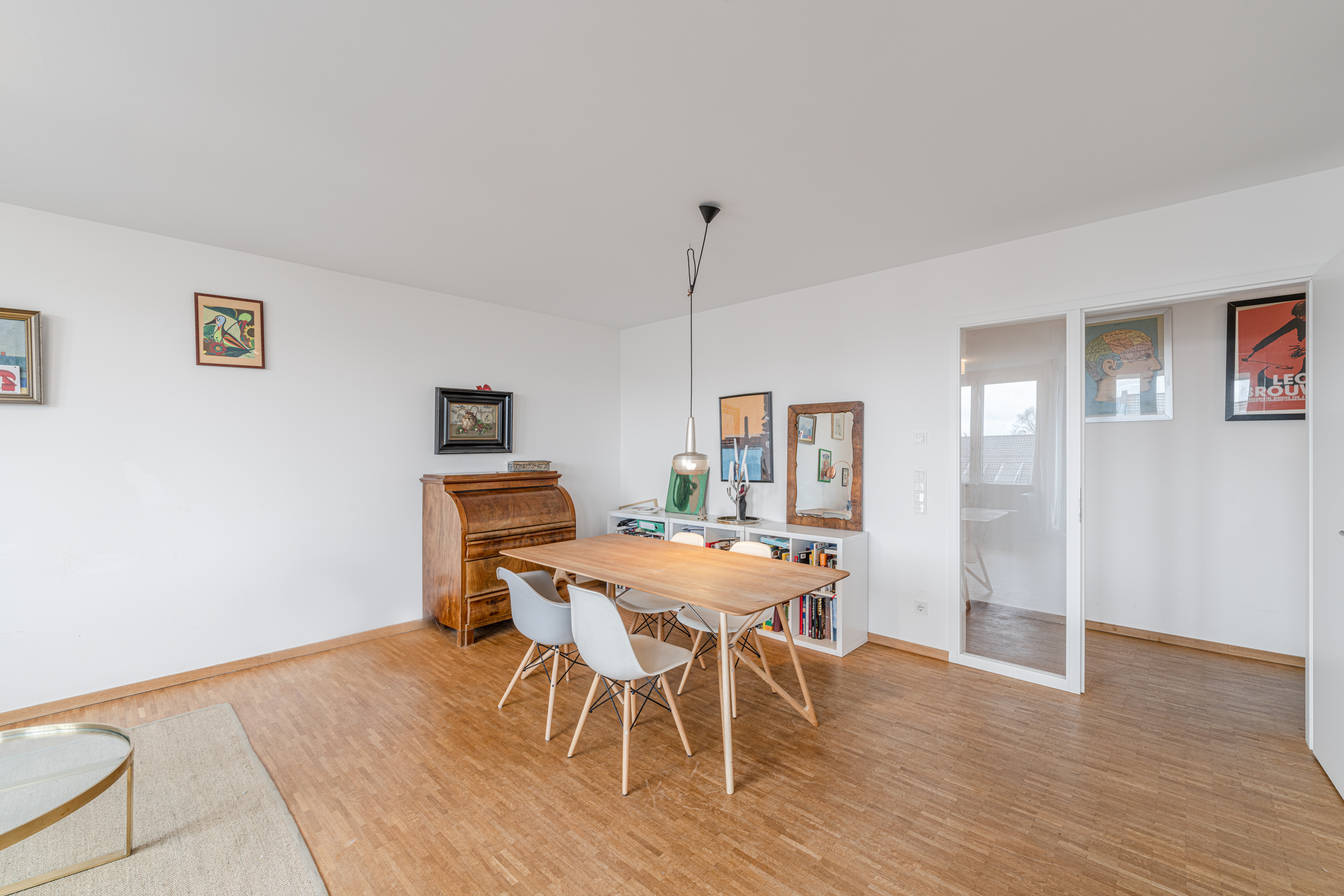 Essbereich mit Holztisch, vier weißen Stühlen, Hängelampe und Bildern an der Wand.