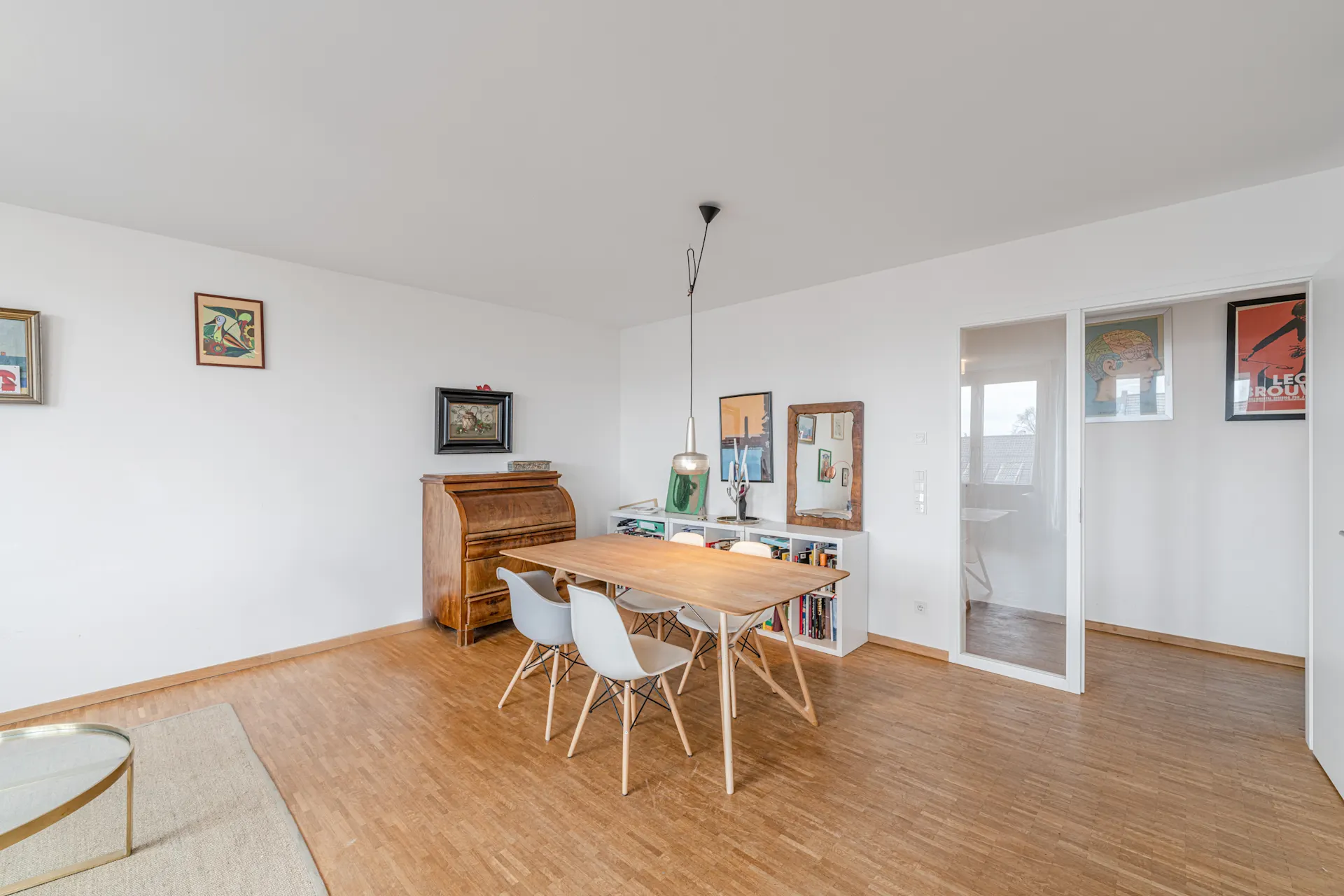 Essbereich mit Holztisch, vier weißen Stühlen, Hängelampe und Bildern an der Wand.