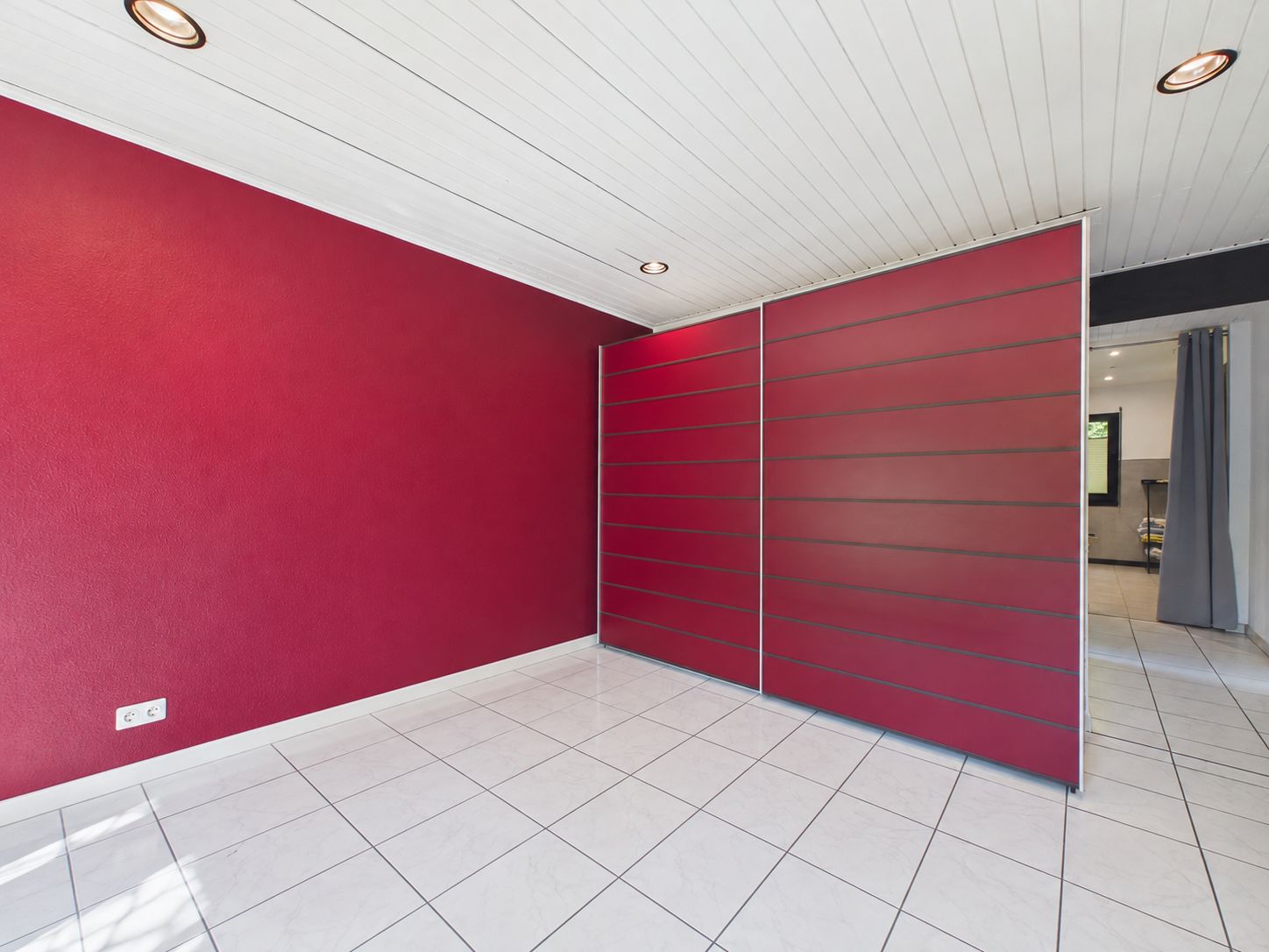 Leerer Raum mit weißem Fliesenboden und roter Wand, weiße Decke und rote Trennwand.