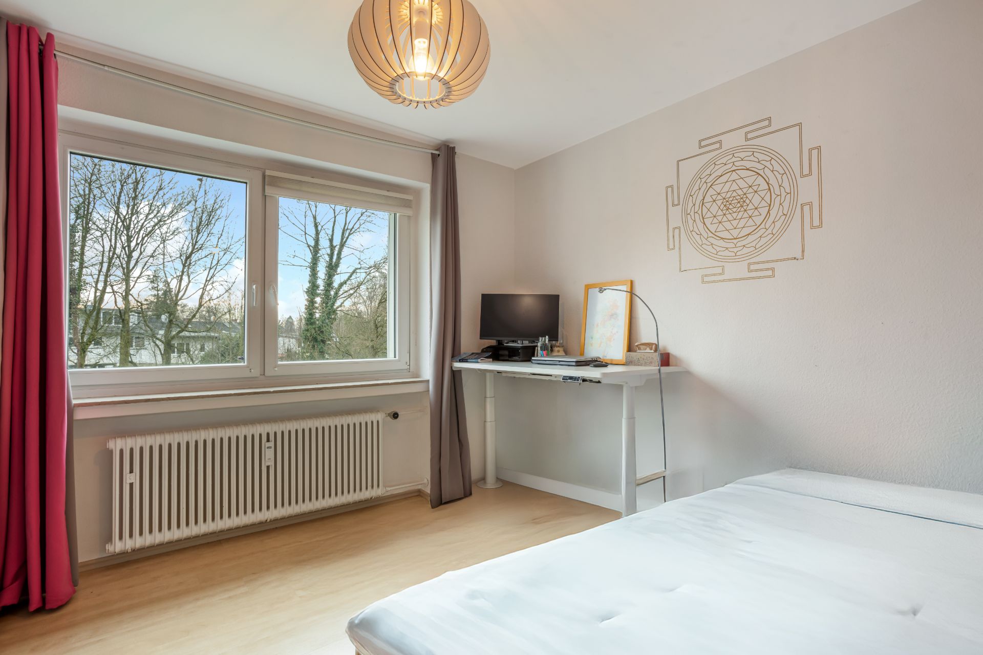 Helles Schlafzimmer mit Schreibtisch, Bett, Fenster mit Blick ins Grüne und Wanddekoration.