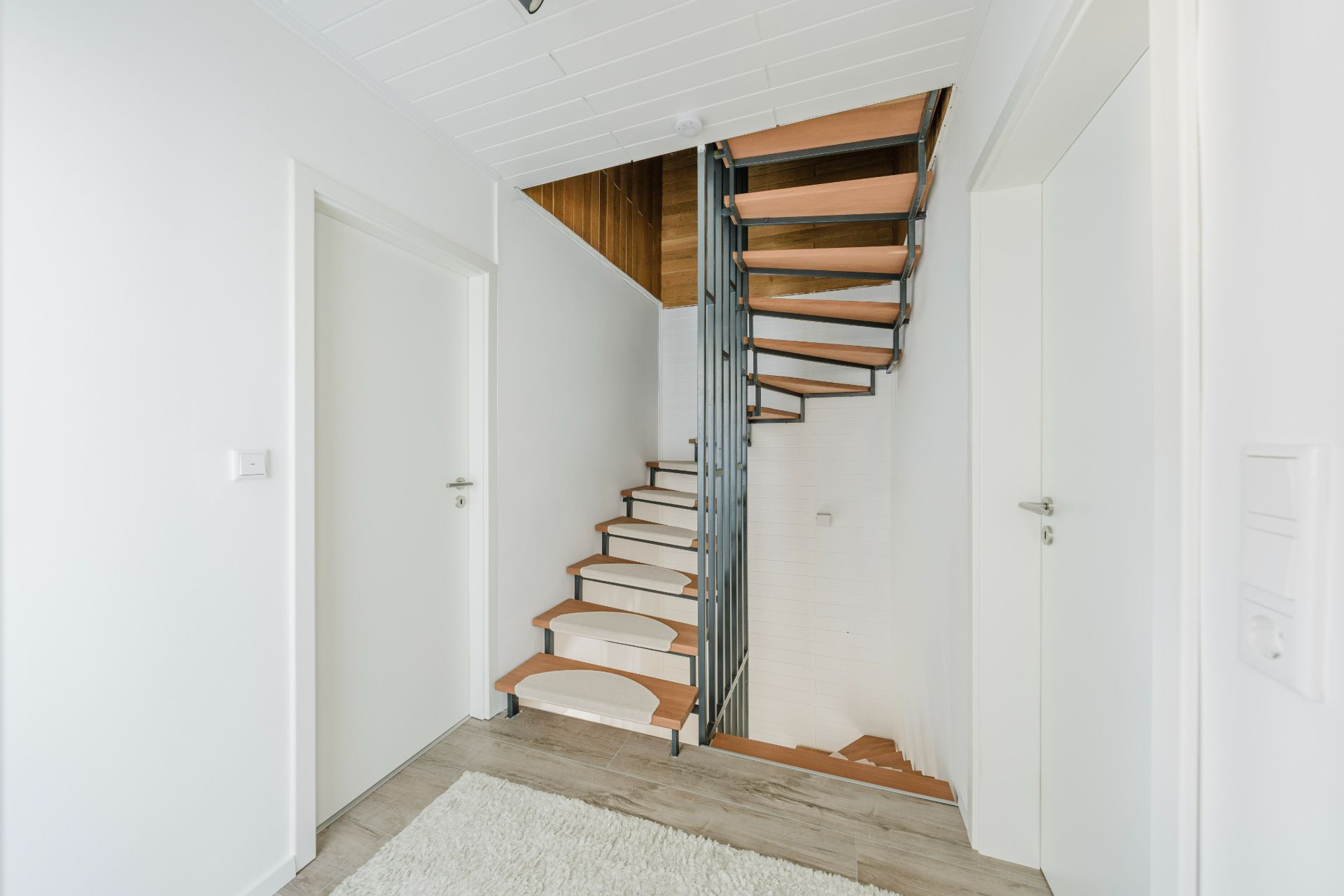 Heller Flur mit moderner Holztreppe und zwei weißen Türen.