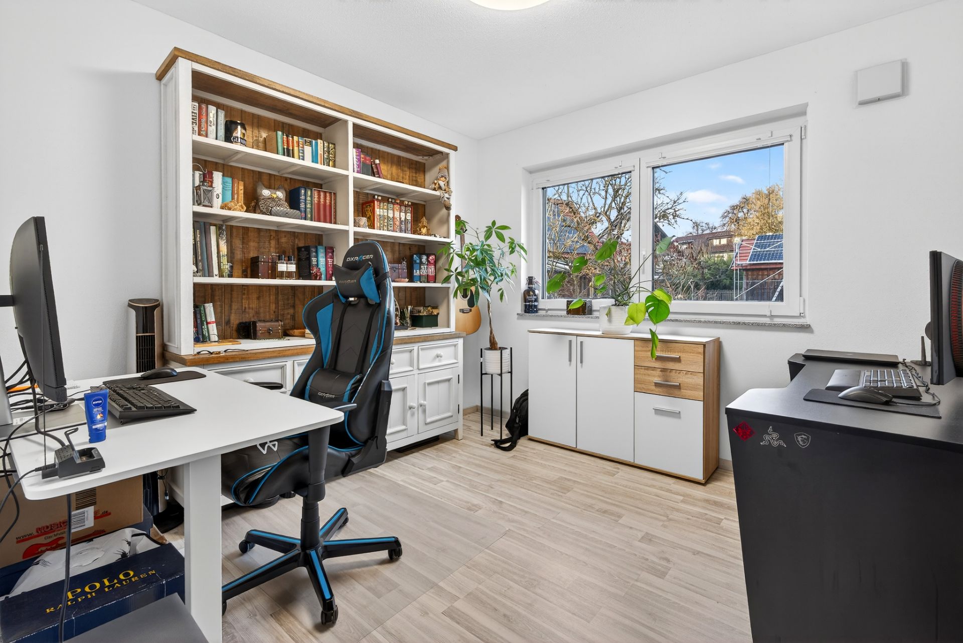 Helles Arbeitszimmer mit zwei Schreibtischen, Bücherregal und Fenster mit Blick nach draußen.