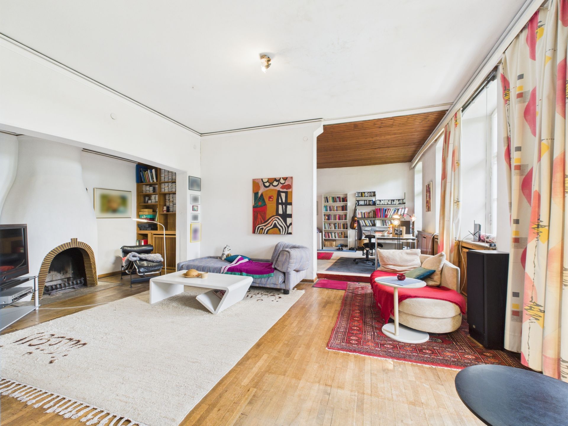 Helles Wohnzimmer mit Kamin, Sofas, Couchtisch, Teppichen und Bücherregalen.