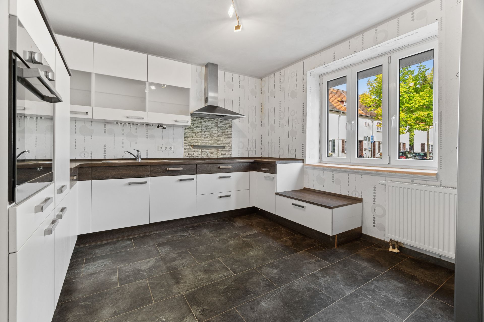 Moderne Einbauküche mit weißen Schränken und großem Fenster mit Blick nach draußen.