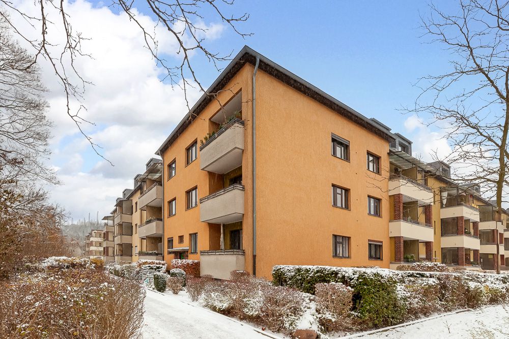 Mehrfamilienhaus mit gelber Fassade und Balkonen, umgeben von schneebedeckten Büschen.