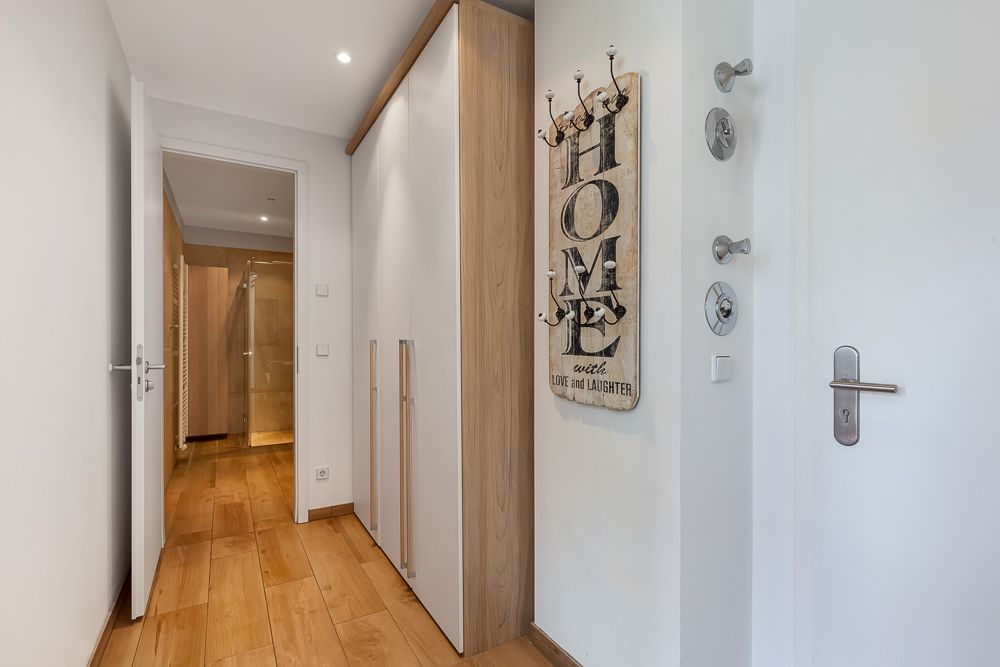 Heller Flur mit Holzfußboden, Garderobenschrank und einem Wandhaken mit Schriftzug.