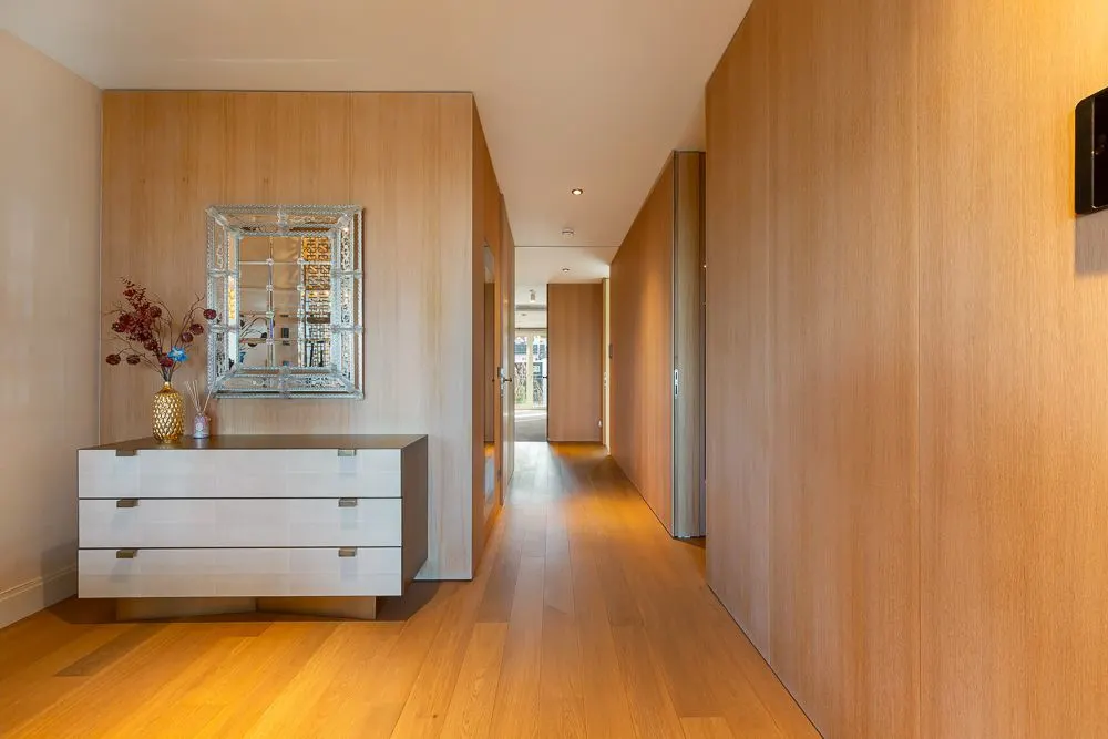 Heller Flur mit Holzverkleidung, Kommode, Spiegel und Vase mit Dekozweigen.