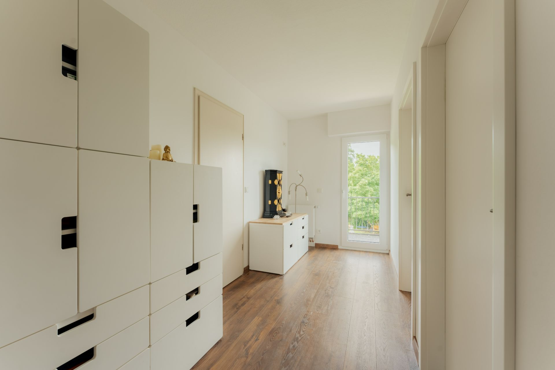Heller Flur mit weißen Schränken, Holzfußboden und Tür zu einem Balkon mit Blick ins Grüne.