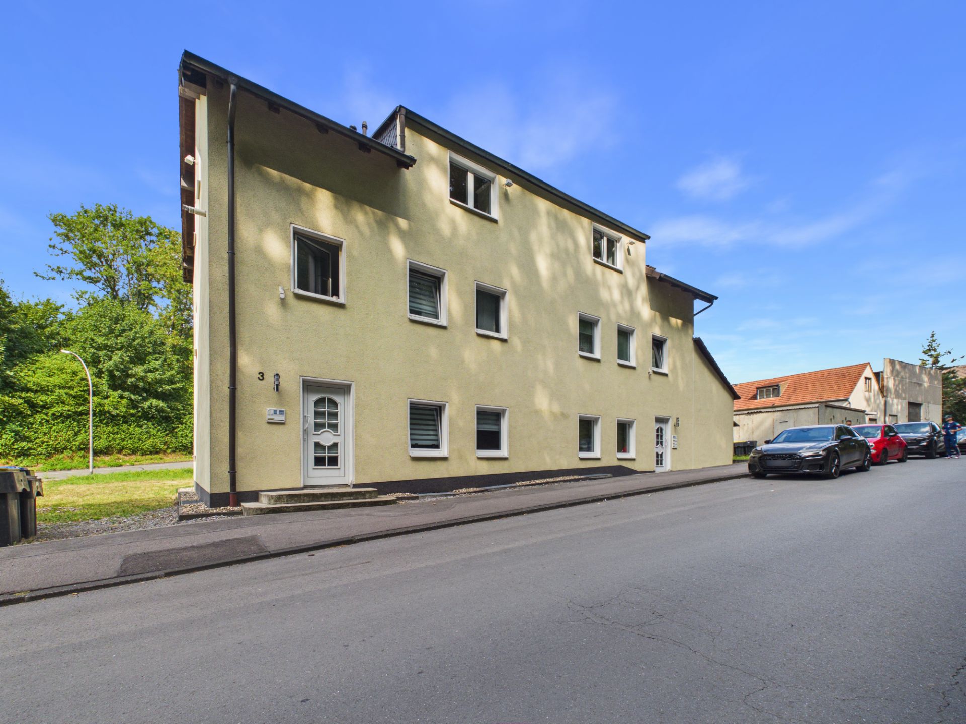 Gelbes Wohngebäude mit mehreren Fenstern an einer ruhigen Straße, Autos am Straßenrand geparkt.