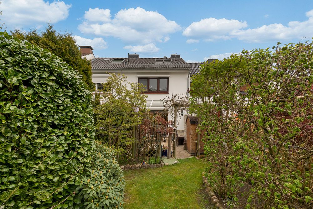 Garten mit Rasen, Sträuchern und Blick auf ein weißes Wohnhaus mit Terrasse.