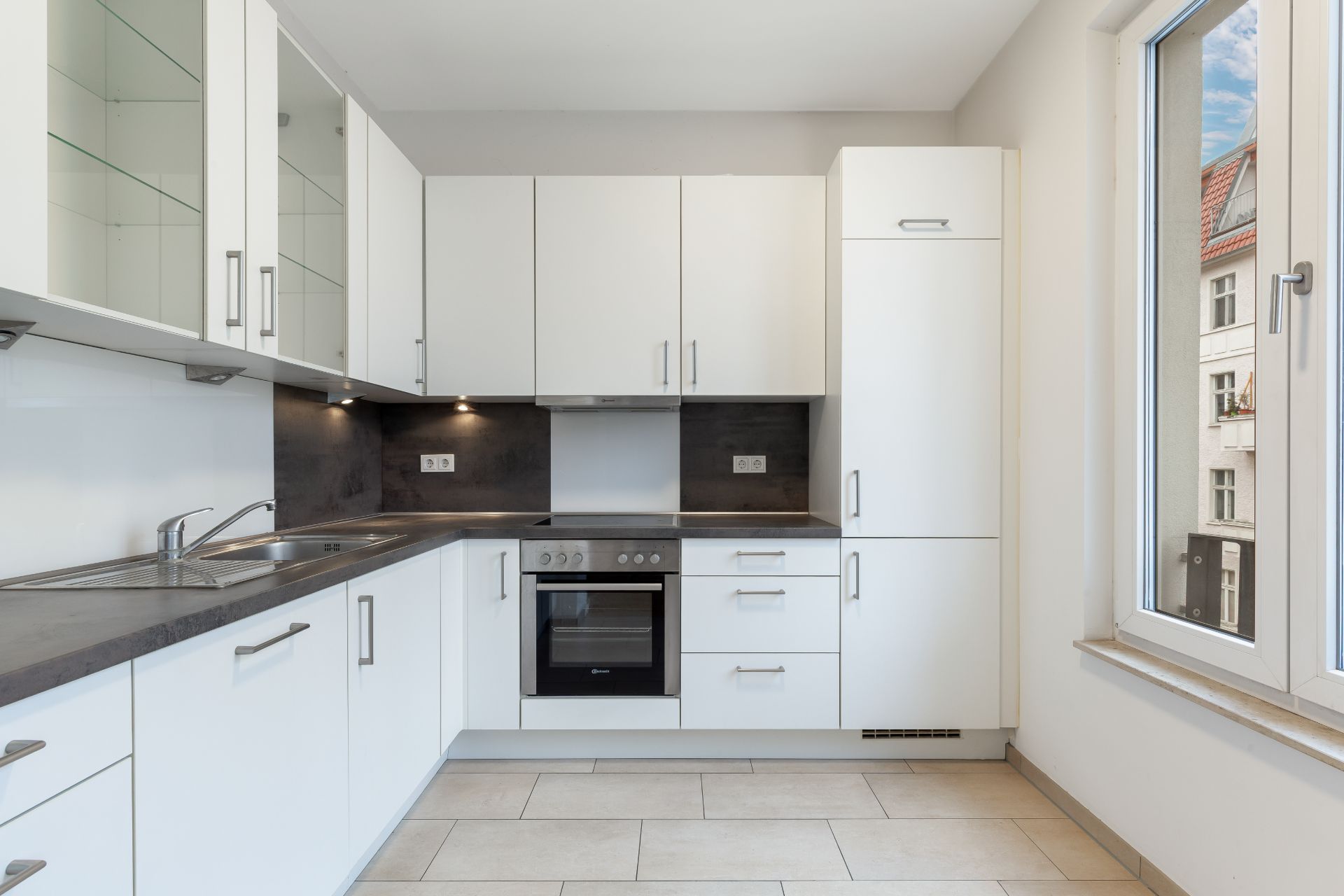 Moderne Einbauküche mit weißen Schränken, Herd, Spüle und Fenster.