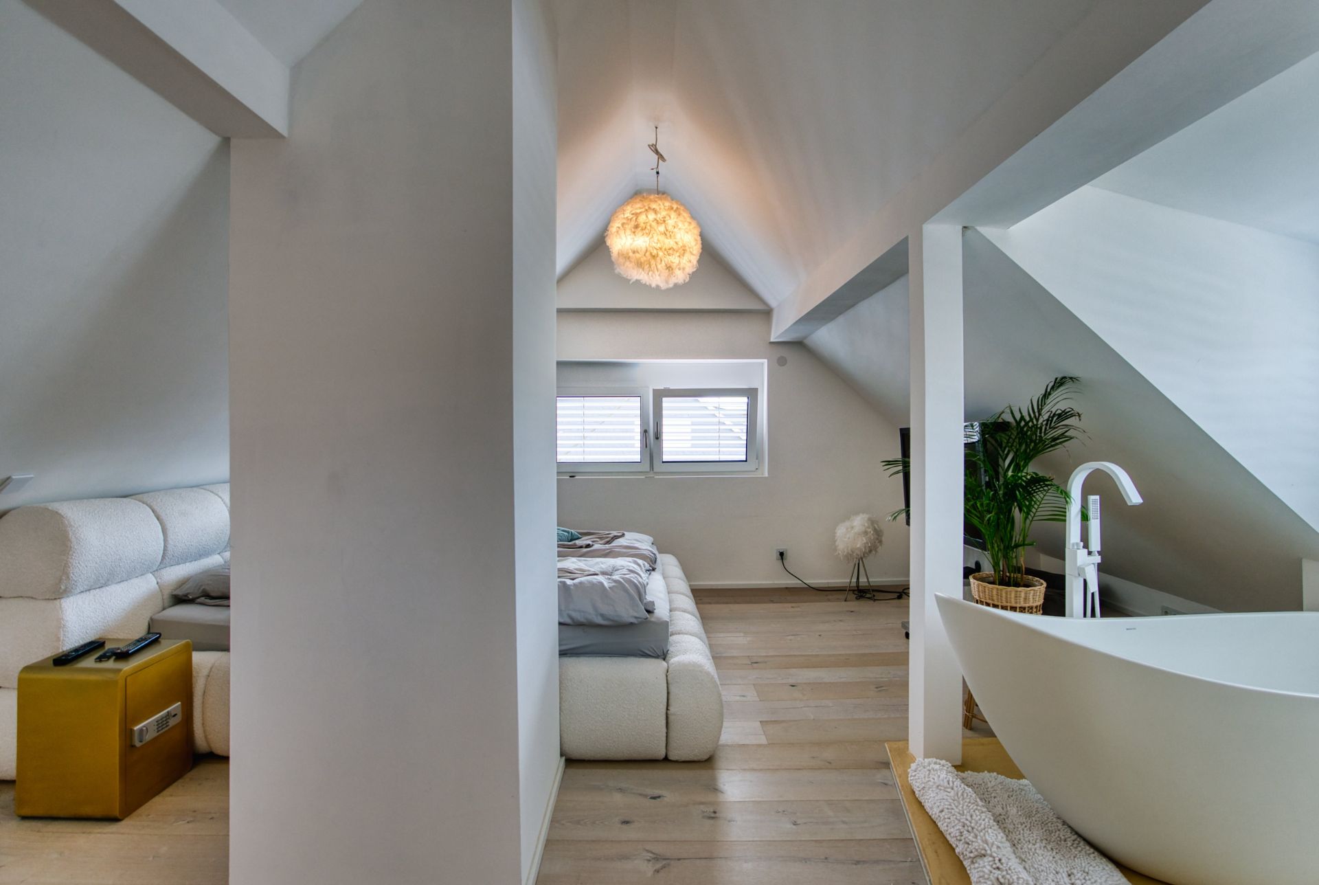 Modernes Schlafzimmer im Dachgeschoss mit freistehender Badewanne und Zimmerpflanze.