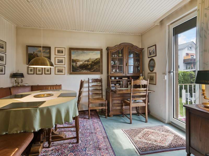 Gemütliches Wohnzimmer mit Holztisch, Vitrine, Stühlen, Teppich und vielen Bildern an der Wand.