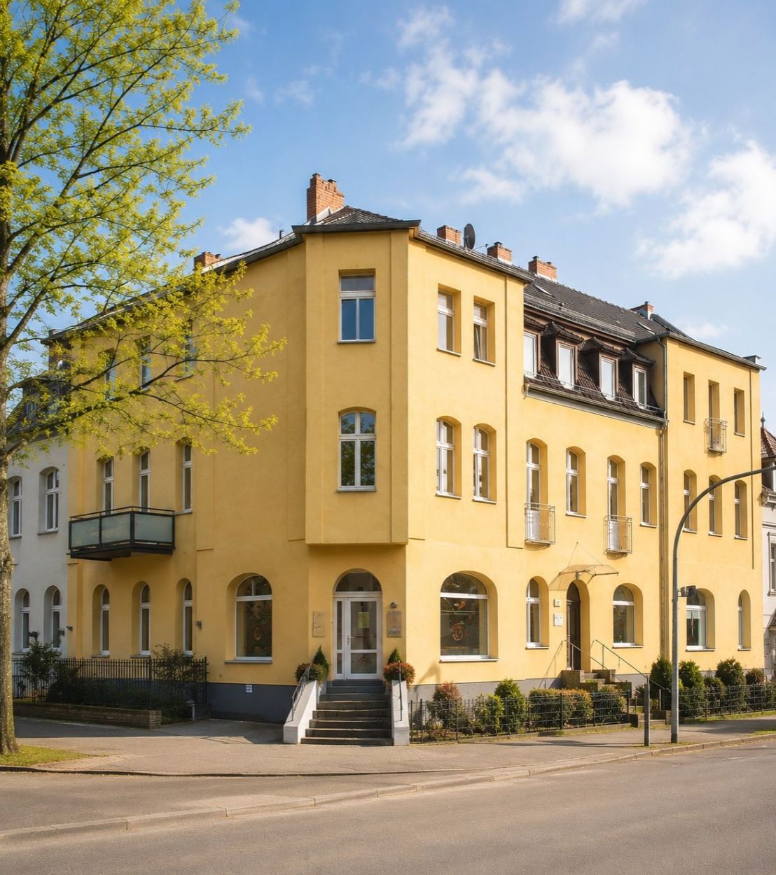 Gelbes Wohnhaus an einer Straßenecke mit mehreren Etagen und Fenstern.