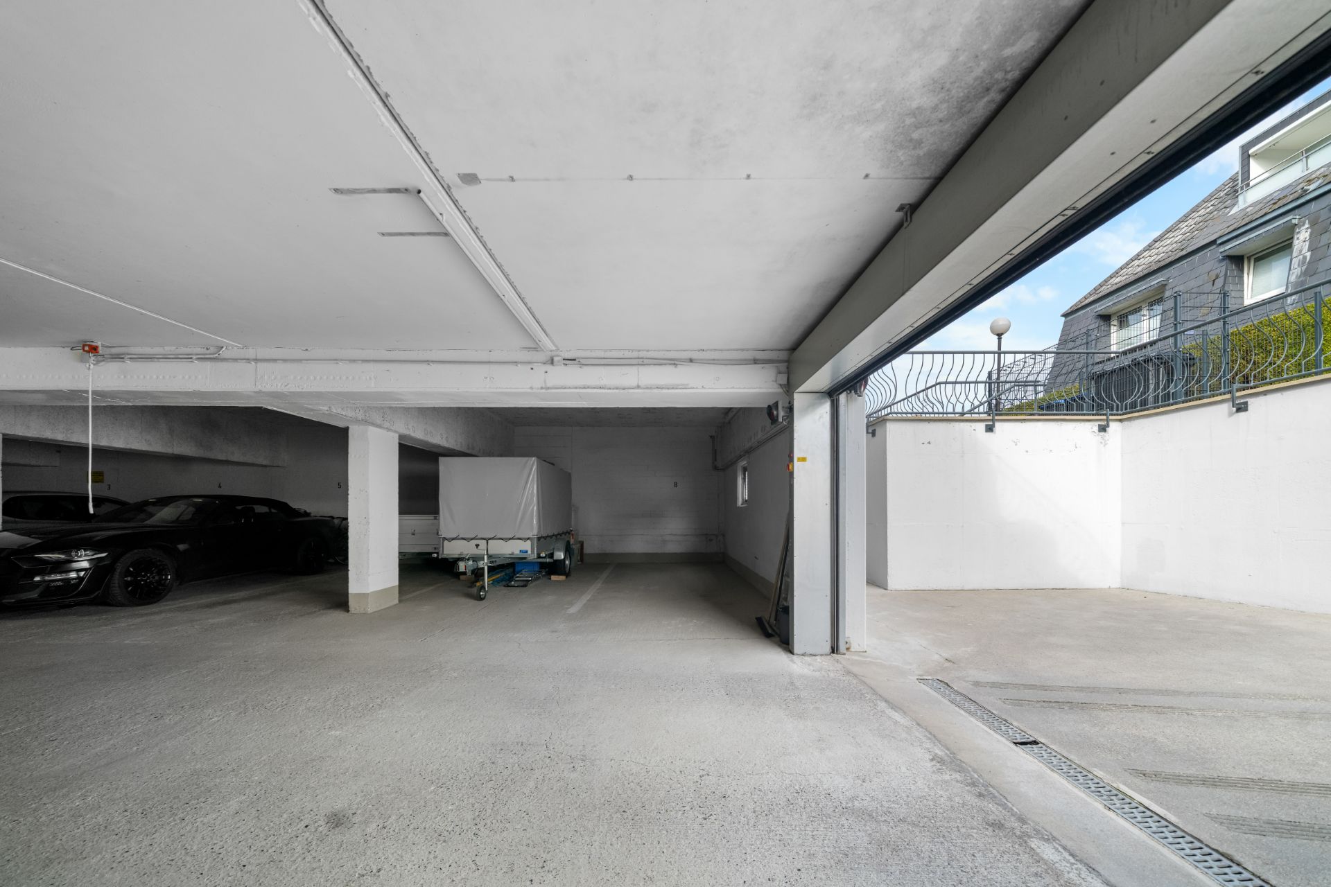 Offene Tiefgarage mit Autos und Anhänger, Einfahrt nach draußen rechts sichtbar.