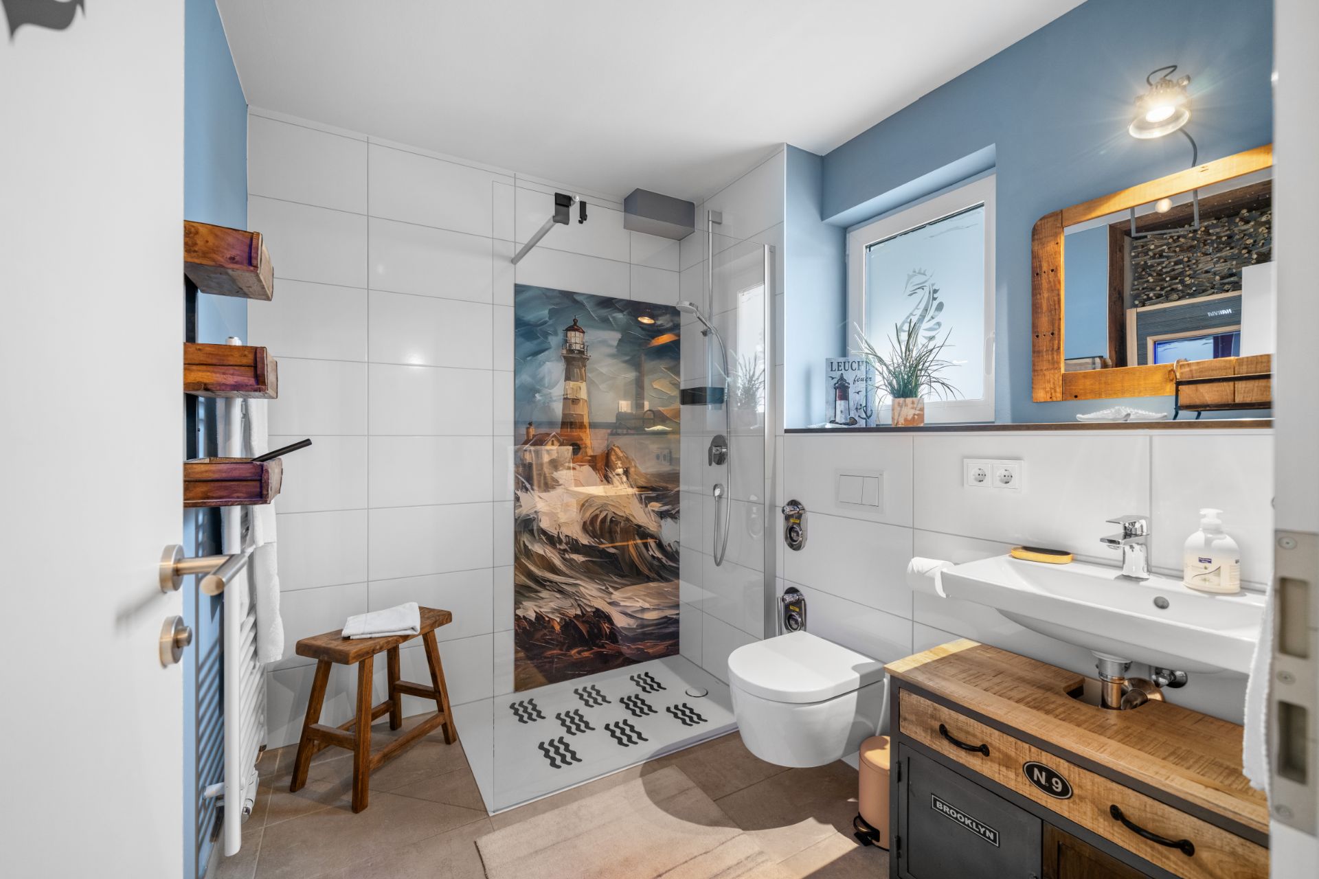 Modernes Badezimmer mit offener Dusche, Leuchtturm-Motiv, Holzstuhl, WC und Waschbecken.