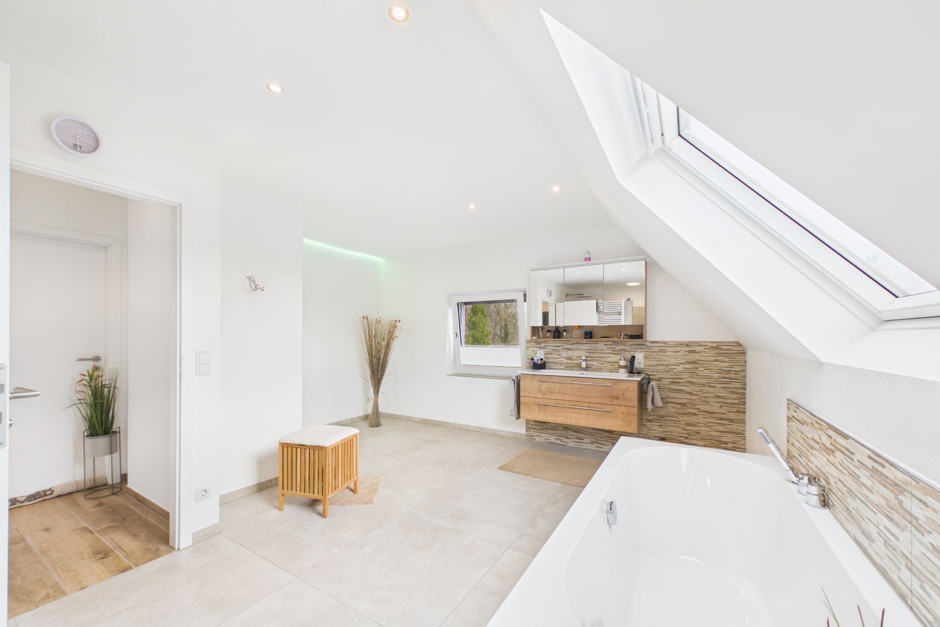 Modernes, helles Badezimmer mit Badewanne, großem Fenster, Holzwaschtisch und Hocker.