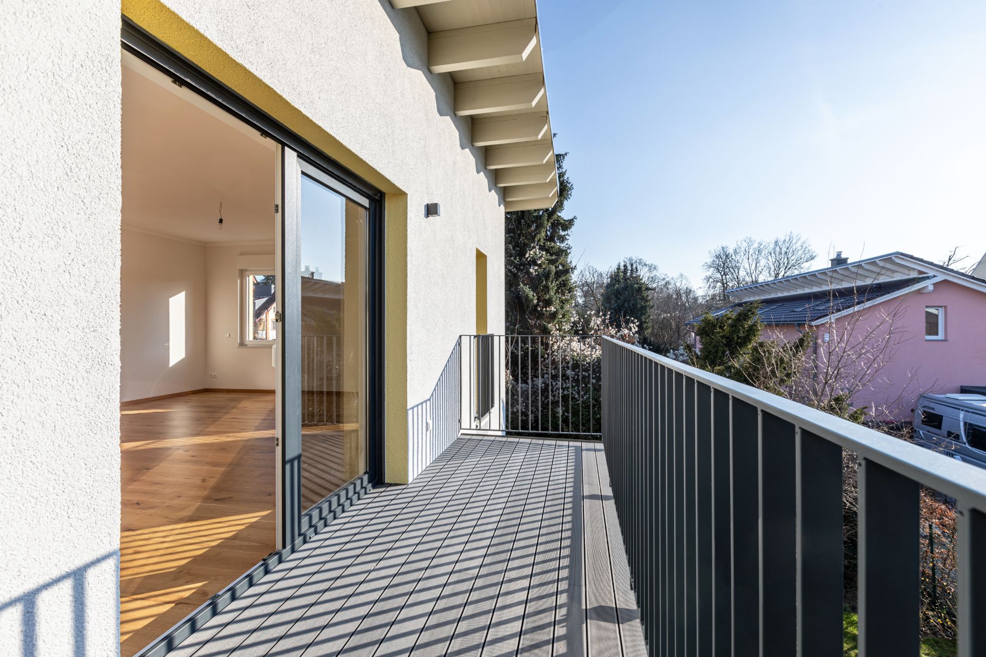 Balkon mit Metallgeländer und Zugang zu einem hellen Zimmer mit Holzboden.