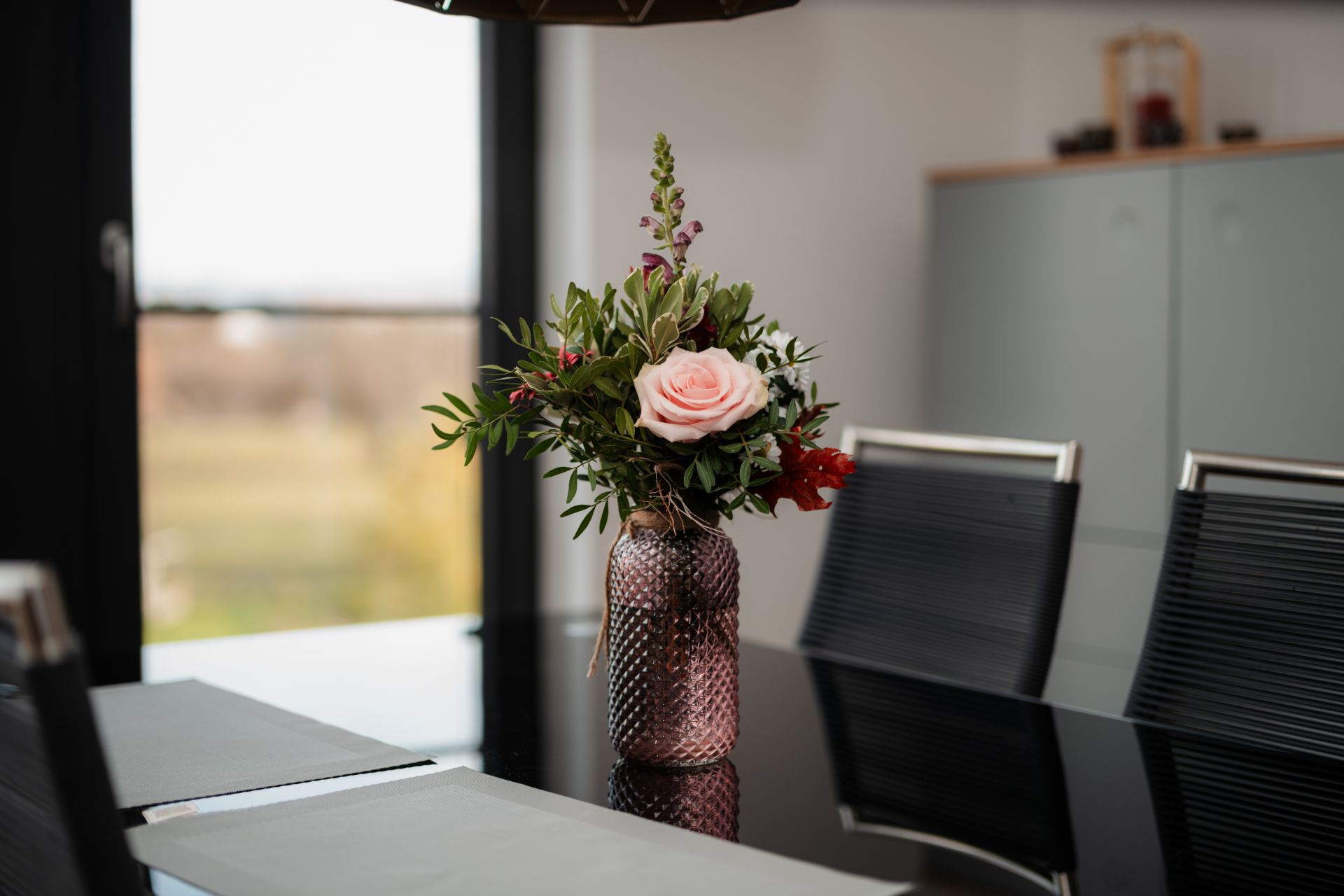 Blumenstrauß in einer Vase auf einem Esstisch mit schwarzen Stühlen.