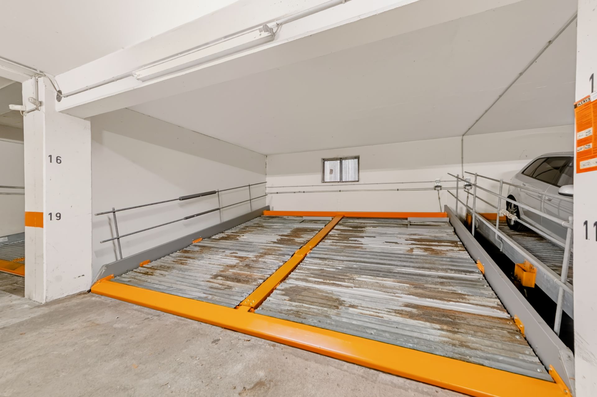 Leerer Parklift mit Metallboden und orangefarbenem Rahmen in einer Tiefgarage.