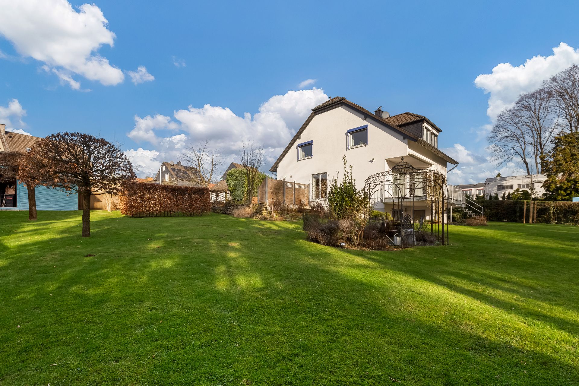 Freistehendes Wohnhaus mit großem Garten, einzelnen Bäumen und blauen Himmel im Hintergrund.