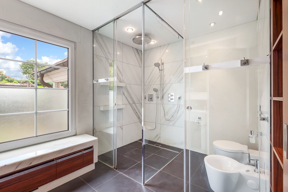Modernes Badezimmer mit großer Glasdusche, Bidet, Toilette und Fenster mit Blick nach draußen.